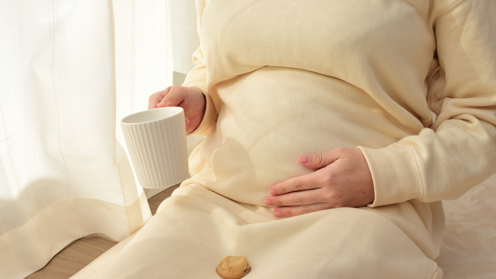 Mujer embarazada tomando agua o comiendo una galleta de jengibre en un entorno tranquilo.