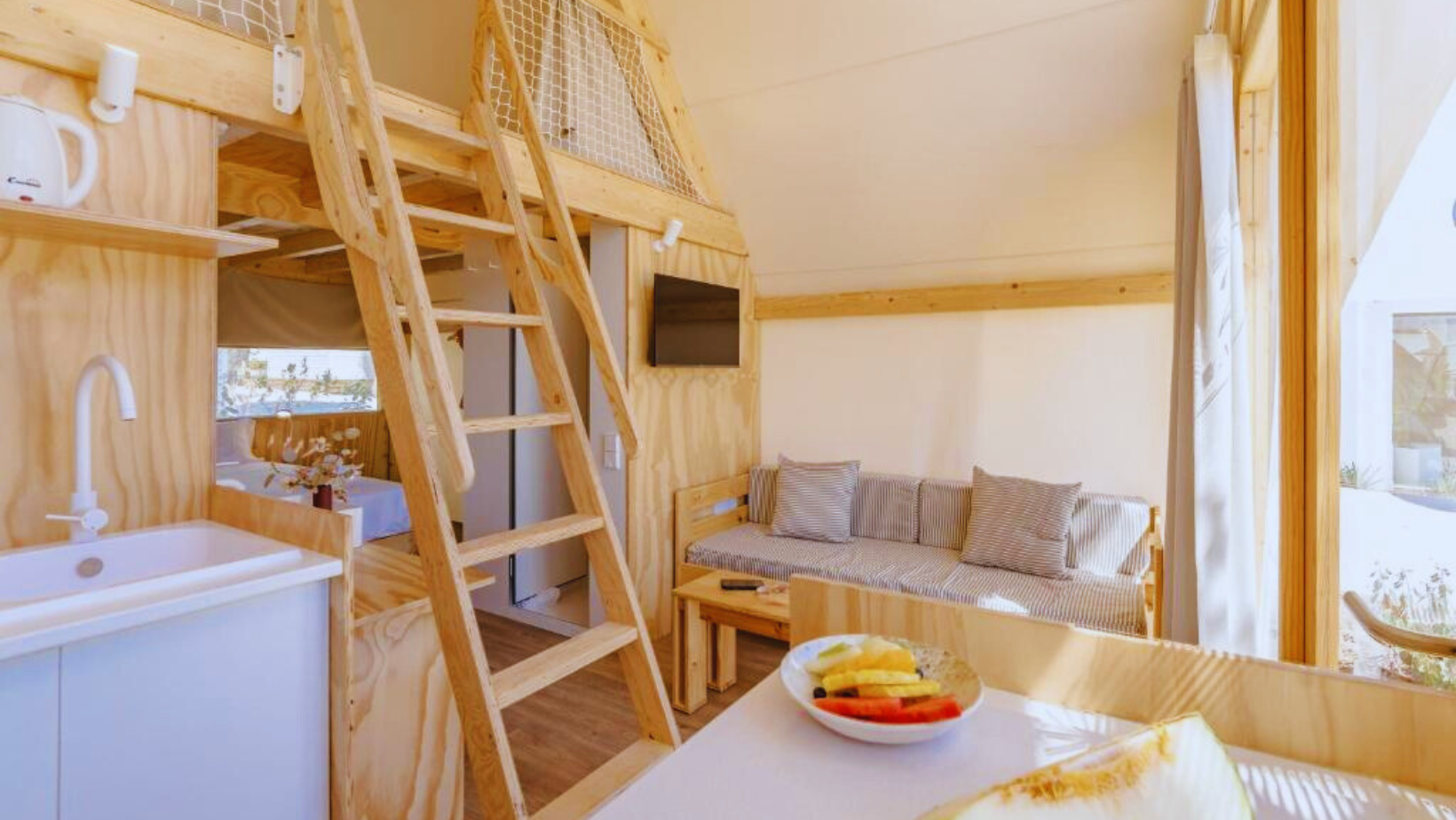 Interior de una tienda safari de lujo en Costa del Sol Glamping Village con vistas a la piscina y terraza de madera.